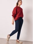Model in een rode sweater en donkerblauwe joggingbroek met trekkoord, posed met gouden sneakers.