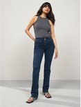 Model draagt een donkerblauwe spijkerbroek met bootcut pasvorm en slim-fit model. De broek heeft een hoge taille met dubbele knoopsluiting.