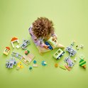 Un enfant est assis parmi des pièces de train LEGO Duplo, dont un train vert clair, des rails, des figurines et un petit chien.