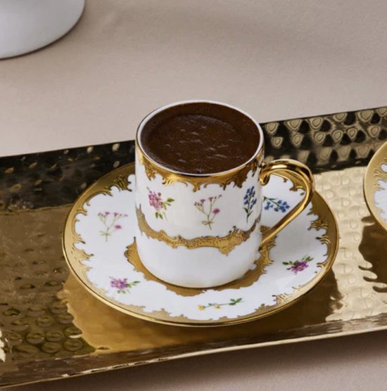 Turks koffiekopje van wit porselein met bloemenmotief en gouden randen op een decoratief gouden dienblad.