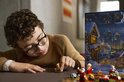 Een jongen met bril bekijkt een LEGO kerstfiguur naast een open adventskalender.