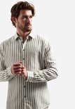 Model in een beige overhemd met verticale, brede witte en taupe strepen, handen gevouwen.