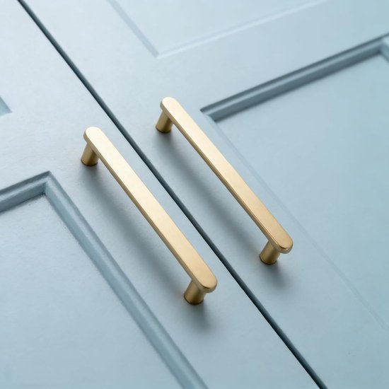 Twee matte messing handgrepen met gouden kleur op zachtblauwe kasten.