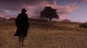 Een man in een lange zwarte jas kijkt uit over een veld met droog gras naar een grote boom bij zonsondergang.