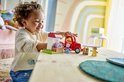Vrolijk kind speelt met LEGO Duplo Peppa Pig tractor en marktkraam op een houten tafel.