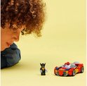 Jongen kijkt naar rode LEGO auto met Spiderman en Wolverine-figuur op gele achtergrond.