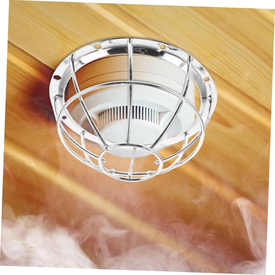 Zilverkleurige metalen beschermkap gemonteerd op rookmelder aan een houten plafond, met rook.