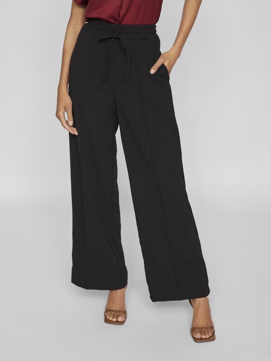 Model met zwarte wijde broek met trekkoord en bordeauxrode top. Broek heeft steekzakken.