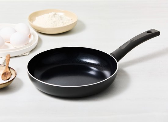 Poêle noire avec un manche ergonomique, à côté d'œufs, de farine et d'herbes.