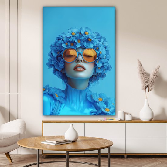 Portrait bleu d'une femme avec des lunettes orange, recouverte de fleurs bleues, accroché à un mur.