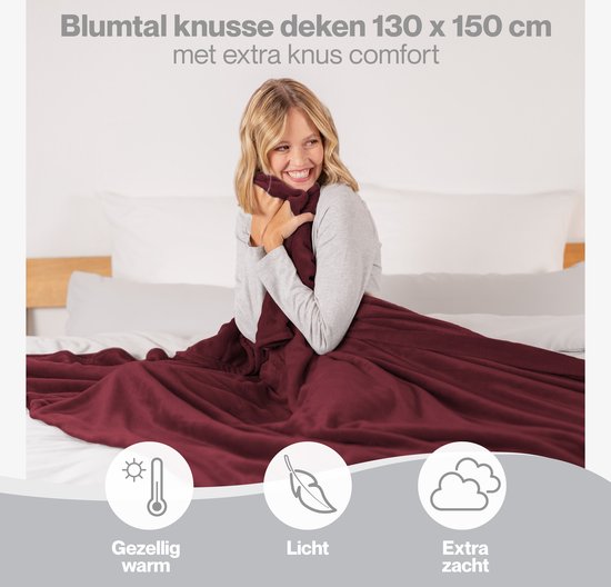 Vrouw omhelst zichzelf met een bordeauxrode deken. Iconen: gezellig warm, licht, extra zacht.