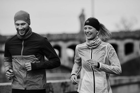 Een lachend hardlopend koppel, mannen met muts en nekwarmer, vrouwen met hoofdband en nekwarmer.