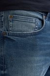 Gedetailleerde close-up van de denim jeans met een klein zakje en klinknagels. Vaal blauwe wassing met lichte beschadigingen.