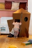 Twee kinderen spelen in een kartonnen raket in een kamer met houten vloer.