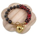 Armband met gouden hartbedel, schakel, rode en zwarte kristallen en zwarte kralen met gouden accenten, geplaatst op een houten display.