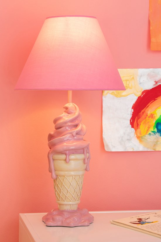 Roze lamp in de vorm van een ijshoorntje met roze softijs, met een roze lampenkap. De lamp staat op een wit bureau.