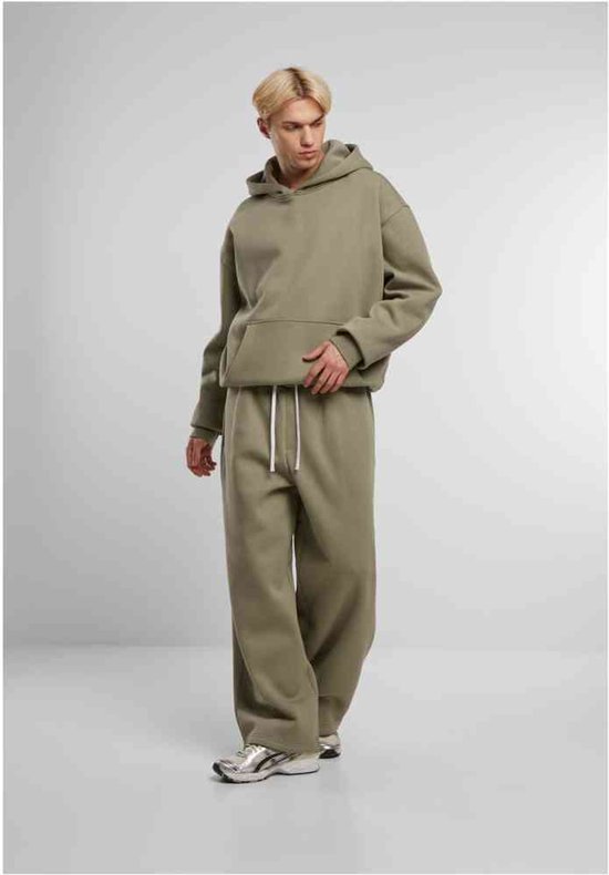 Man draagt een olijfgroene wijde joggingbroek en hoodie met witte trekkoorden.