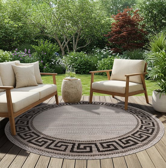 Rond grijs en beige vloerkleed met zigzag patroon op een houten terras.