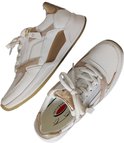 Twee witte sneakers met goudkleurige en taupe accenten, één ligt voor de ander.