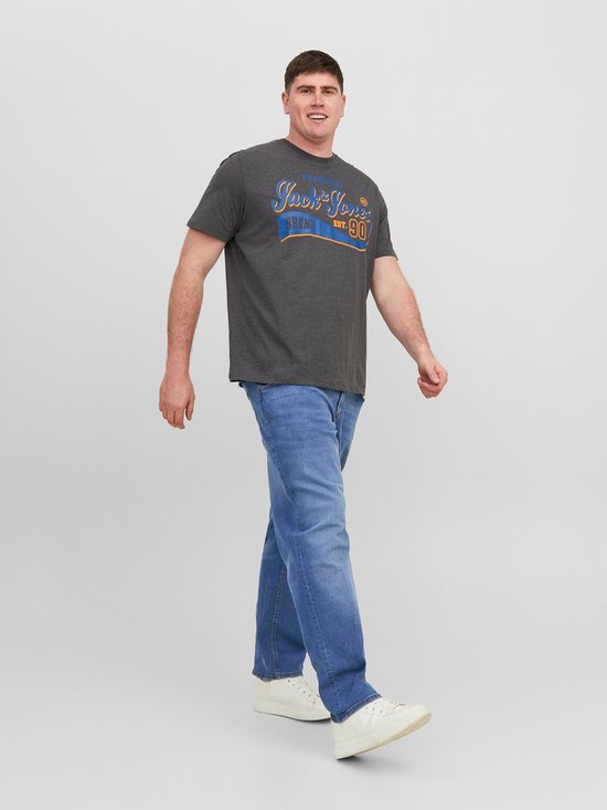 Man loopt naar voren, draagt een grijs t-shirt met tekst en blauwe jeans. Hij draagt witte sneakers.