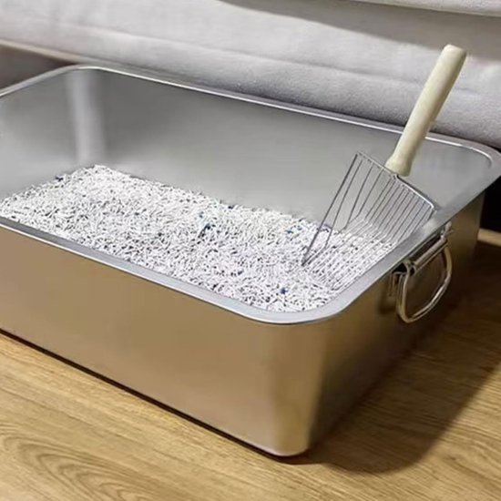 Roestvrijstalen kattenbak met witte korrels en een metalen schep met houten handvat.