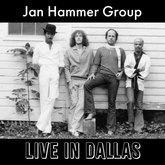 Jan Hammer Group, LIVE IN DALLAS. Vier mannen met kleding uit de jaren '70 staan ​​voor een houten huis. De eerste van links draagt een witte outfit met een hoed. De anderen dragen verschillende kleuren en stijlen kleding.