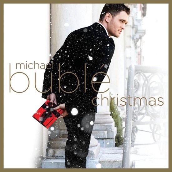 Michael Bublé in zwart pak met strik, houdt rode kerstcadeaubox vast. Sneeuw valt.