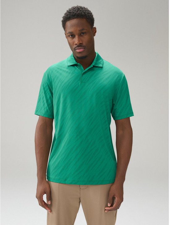 Man draagt groene jacquard poloshirt en beige broek.