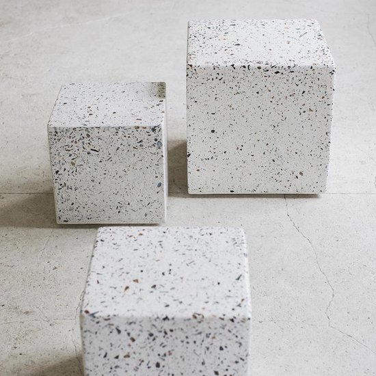 Drie kubusvormige bijzettafels met terrazzo-look in wit met veelkleurige spikkels op betonvloer.