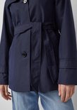 Detail van een donkerblauwe trenchcoat met ceintuur en knoop.