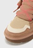 Close-up van de neus van een bruine UGG sneaker met suède, mesh en crème details.