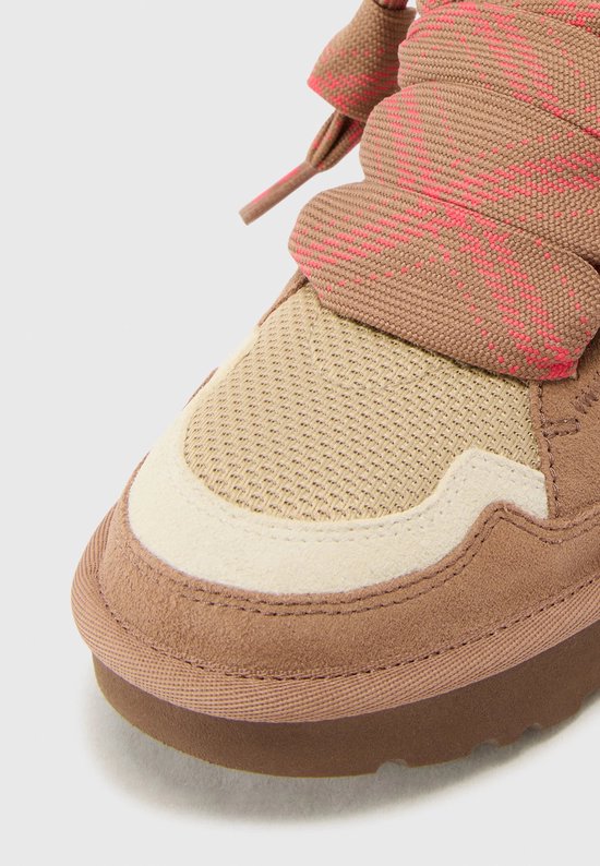 Close-up van de neus van een bruine UGG sneaker met suède, mesh en crème details.