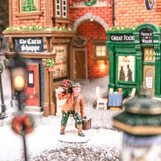 Man met cadeau op zijn schouder en koffer in een besneeuwde winkelstraat.
