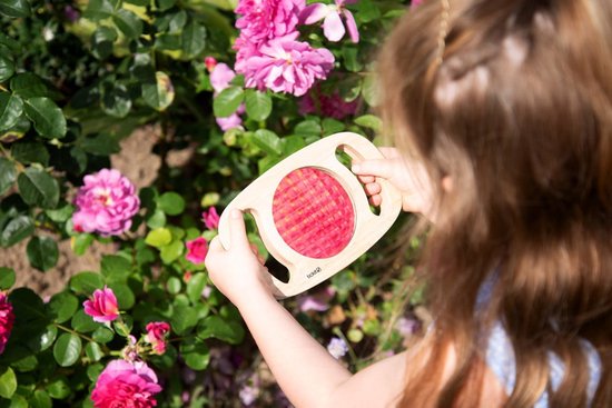 Enfant tenant un kaléidoscope en bois avec des motifs rouges près de roses.