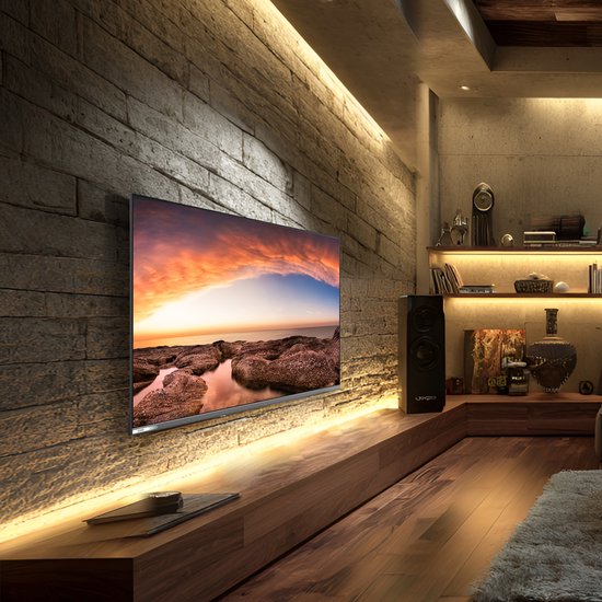 Moderne woonkamer met een grote flatscreen tv die een zonsondergang boven rotsachtige kustlijn toont. Sfeervolle verlichting.