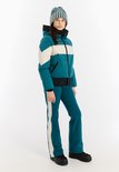Meisje draagt een turquoise ski-jas met beige en witte strepen en een bijpassende muts.