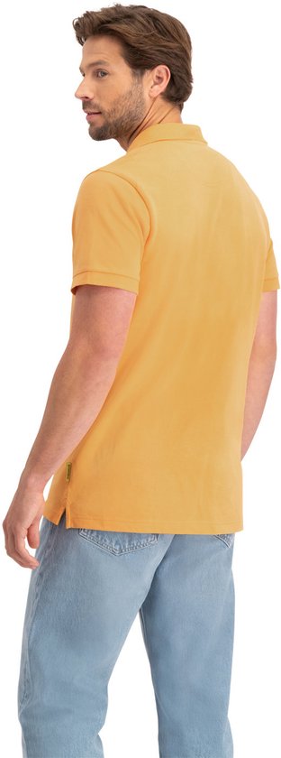 Man met zomers oranje poloshirt met korte mouwen en lichtblauwe jeans, kijkend naar de zijkant.