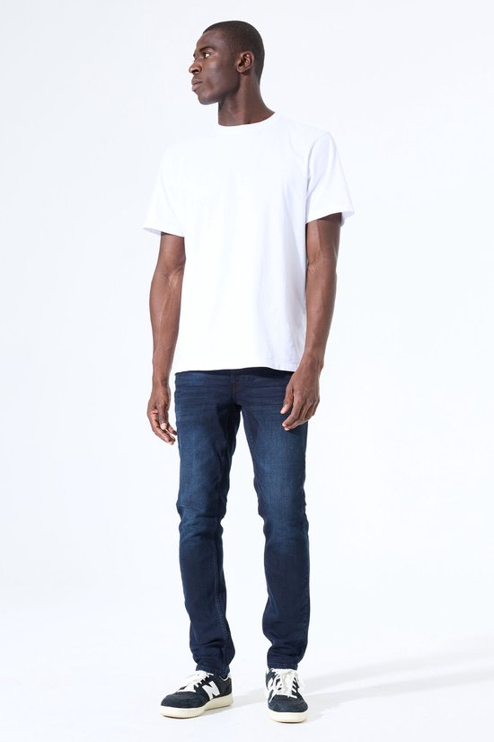 Man met donkere jeans en wit t-shirt, sneakers, staand.
