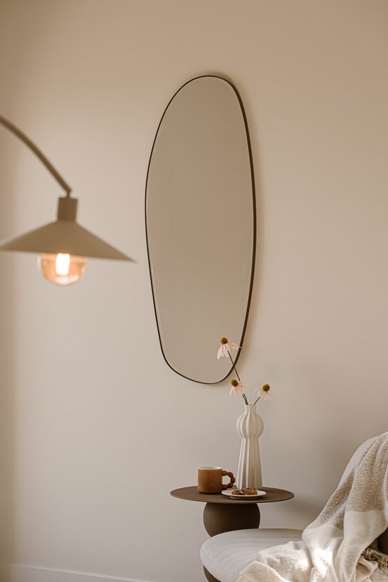 Een organische spiegel aan de muur met een lamp, mok, koekjes en bloemen.