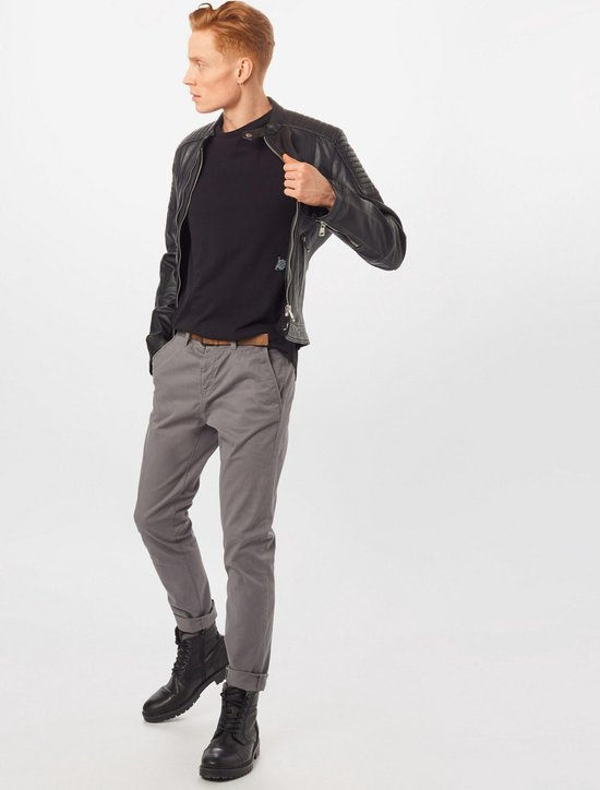 Man in grijze chino met bruine riem, zwart T-shirt en leren jack.