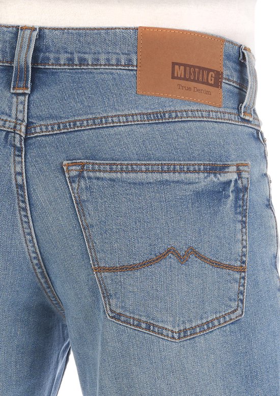 Close-up van de achterkant van een spijkerbroek met een bruin Mustang label en kenmerkende stiksels op de zakken.
