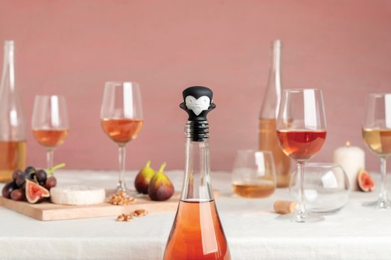 Een rosé wijnfles met een speelse vampier-wijnstopper, op een tafel met diverse glazen en fruit.