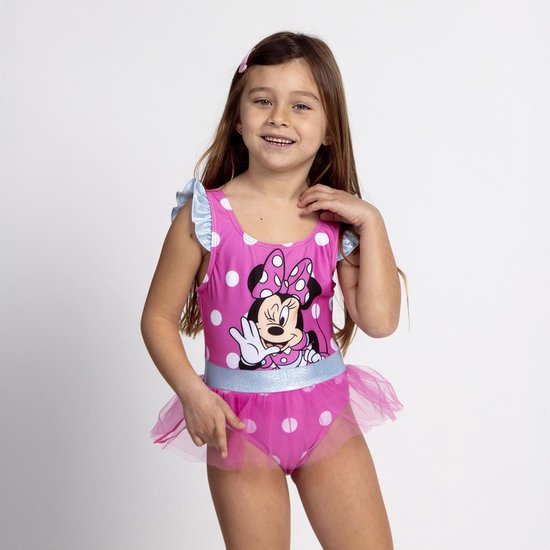 Een meisje met lang bruin haar draagt een roze badpak met witte stippen, Minnie Mouse print en tule rokje.