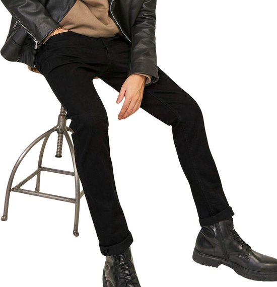 Man zittend in zwarte jeans, zwarte leren jas en beige hoodie, met zwarte laarzen.