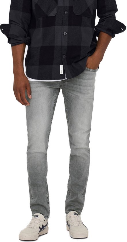 Man met de hand in de zak van een grijze slim fit jeans, met een geruit overhemd.