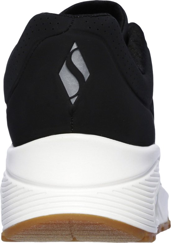 Achterkant van een zwarte sneaker met witte zool en een reflecterend logo op de hiel.