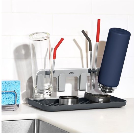 Bouteille bleu marine, en verre et rose, et accessoires sur un égouttoir gris foncé avec un fond de carrelage blanc.