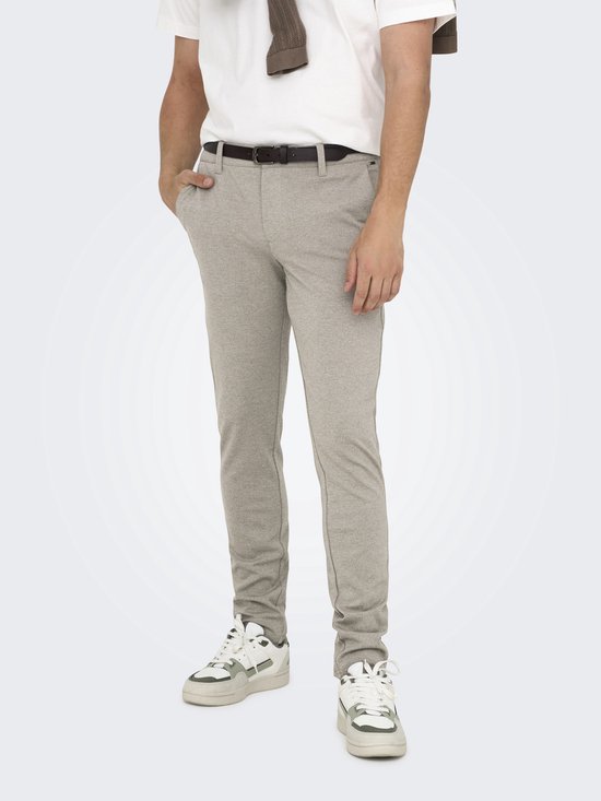 Man in een beige chino, wit T-shirt, bruine riem en witte sneakers. Detail van de broekspijpen.