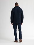 Man staand op rug gezien, met donkerblauwe peacoat, jeans en bruine schoenen.