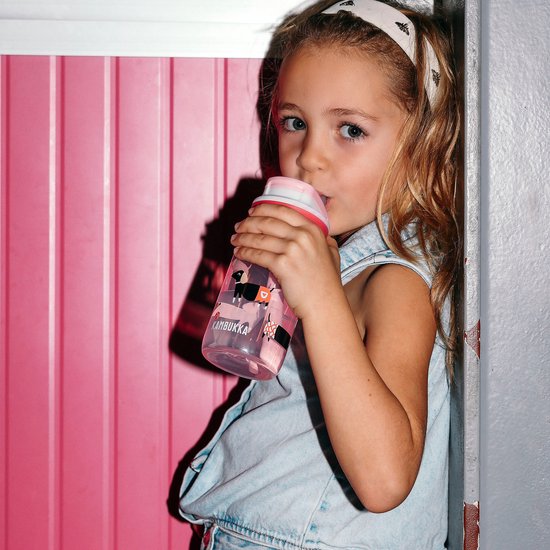 Une fille aux cheveux blonds boit dans une bouteille Kambukka rose avec un imprimé de chiens.